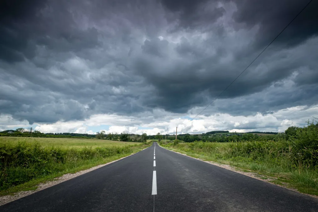 Beautiful view of an empty road surrounded by greenery under dark storm clouds - Times of Dubai Uae weather alerts rain dust and safety warnings as uae weather shifts suddenly times of dubai