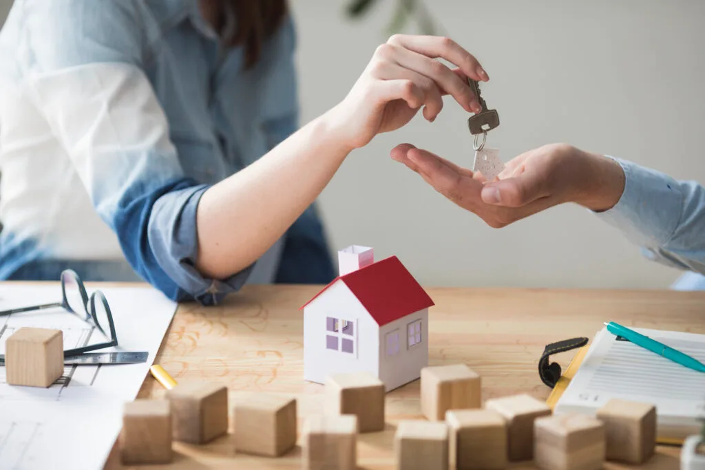close-up-woman-s-hand-giving-house-key-man-wooden-table - Times of Dubai Dubai first time home buyers discount developers offer special rates times of dubai